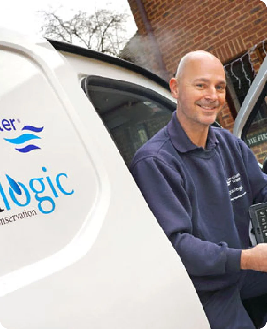 A smiling Aqualogic worker stands next to a company van holding equipment.