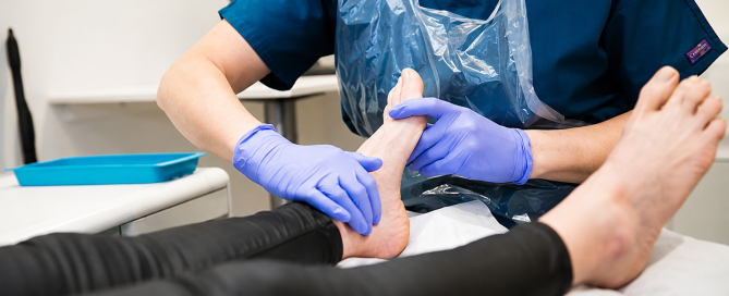 Podiatrist performing a biomechanical foot assessment by examining a patient's ankle and foot during a consultation.